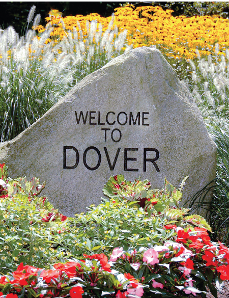 Large rock surrounded by flowers with welcome to Dover engraved on it