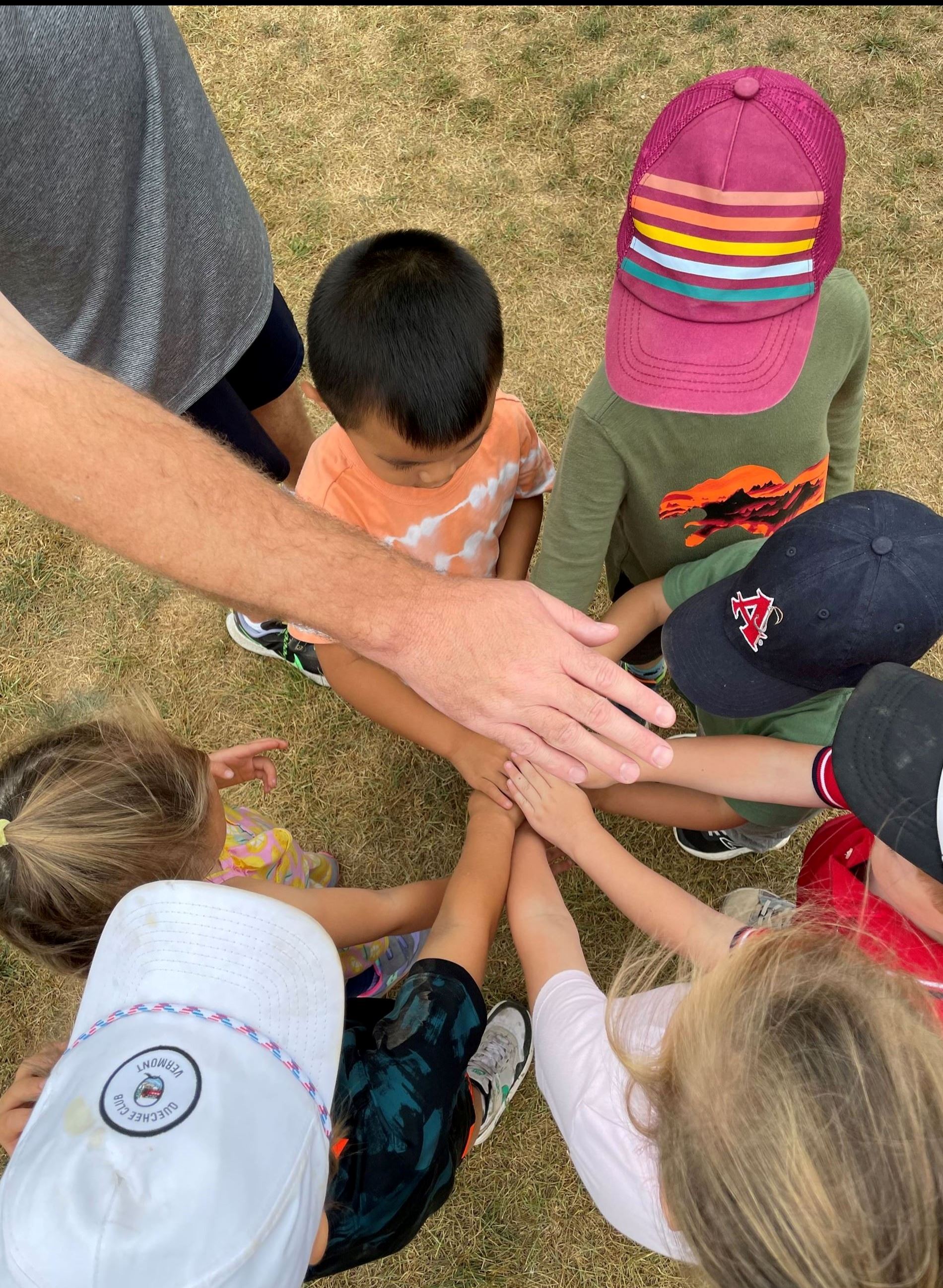 Photo of children in huddle to end the day with all hands in the middle